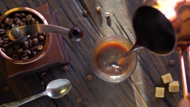 Freshly brewed coffee from cezve is poured into a coffee cup. Steam comes out of the cup, an old coffee grinder is in the composition. 4K video.