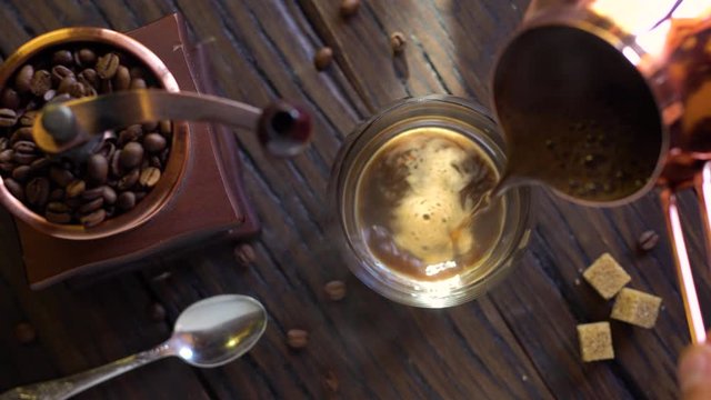 Freshly brewed coffee from cezve is poured into a coffee cup. Steam comes out of the cup, an old coffee grinder is in the composition. 4K video.