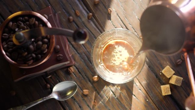 Freshly brewed coffee from cezve is poured into a coffee cup. Steam comes out of the cup, an old coffee grinder is in the composition. 4K video.