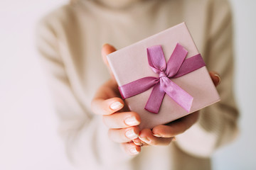 Female hands holding pastel coloured present with pink ribbon. Festive backdrop for holidays: Christmas, New Year, Birthday, Valentines day.