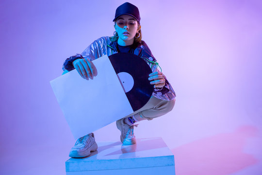 The girl with the vinyl record. Colored background and neon light. Modern clothes. Music poster. Retro concept.