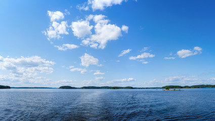 Back view of motor boat cruising on calm water, overlooking islands and blue sky. Lake Saimaa, Finland.