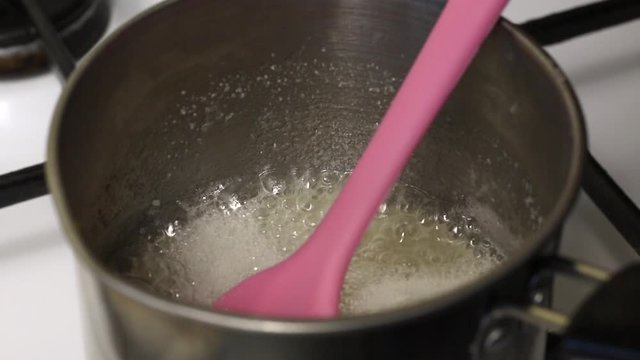 Syrup is boiled in a stewpan to prepare a marshmallow. Visible thick foam. A man mixes the syrup so that it does not burn.