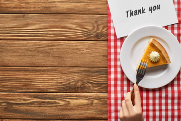 cropped view of woman eating pumpkin pie on plaid napkin with thank you card on wooden table