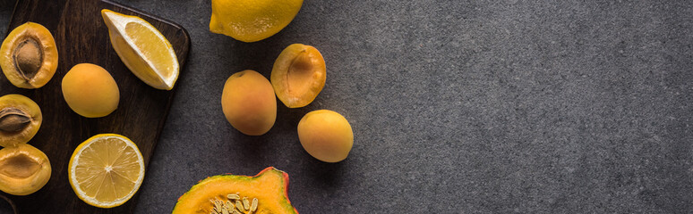top view of pumpkin, apricots and lemon on wooden cutting boards on grey textured background, panoramic shot