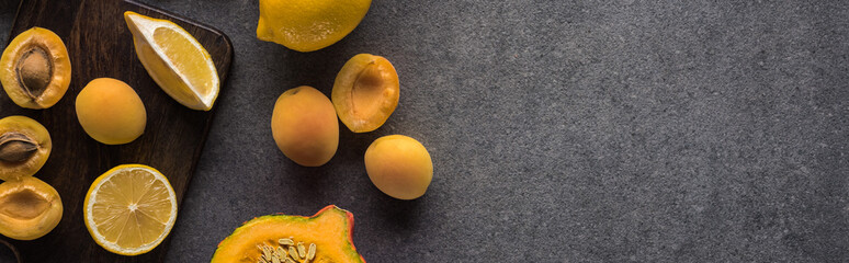 top view of pumpkin, apricots and lemon on wooden cutting boards on grey textured background,...