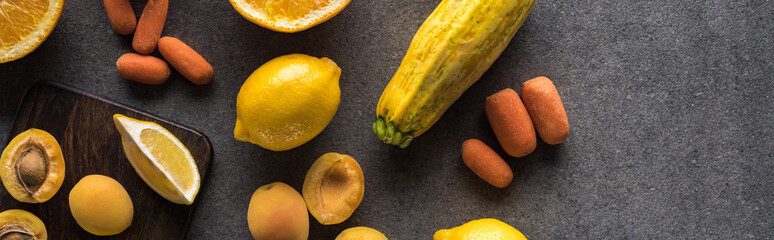 top view of yellow fruits and vegetables on wooden cutting boards on grey textured background,...