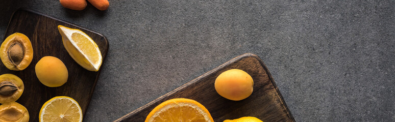 top view of yellow fruits on wooden cutting boards on grey textured background, panoramic shot
