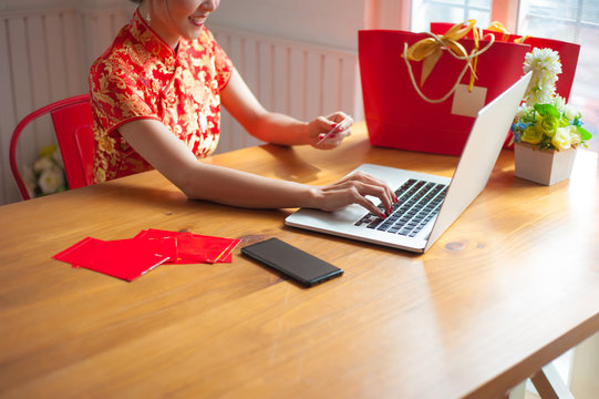 The smiling young woman happily uses a laptop and holds a credit card while shopping online during the Chinese New Year.