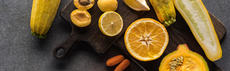 top view of yellow fruits and vegetables on wooden cutting boards on grey textured background,...