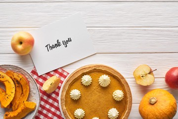 top view of pumpkin pie with thank you card on wooden white table with apples