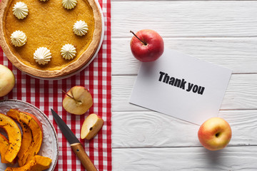 top view of pumpkin pie, ripe apples and thank you card on wooden white table