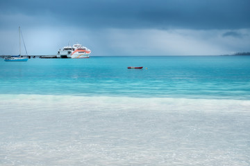 Beautiful light at the horizon on a rainy day at Kuto Bay with a ferry boat at the pier on Isle of Pines in New Caledonia, French Polynesia, South Pacific Ocean.