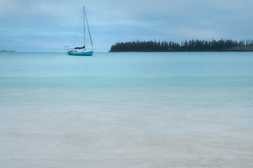 A boat on the water in the clear, pristine waters at Kuto Bay with Pine forests at the horizon in the background on Isle of Pines in New Caledonia, South Pacific ocean.