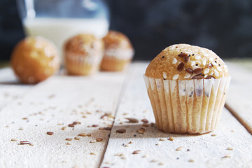 Fairy cakes baked with some sessame seeds on a white wooden table against a black background in a rustic kitchen. Jar of milk at breakfast and empty copy space for Editor's text.