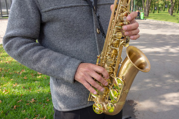 Man plays on saxophone in the park. Street musician with sax performs music for charity. Public...