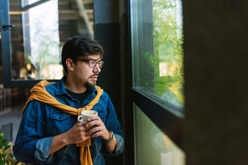 Portrait of young man in front of window drinking coffee