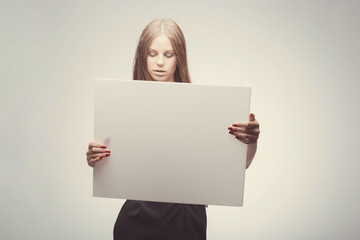 Fashion pretty girl holding white board with place for text. Surprised girl looking serious
