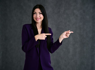 Portrait of a pretty brunette girl with good makeup with long hair on a gray background in a business suit. Stands in different poses with emotions.