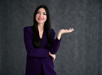 Portrait of a pretty brunette girl with good makeup with long hair on a gray background in a business suit. Stands in different poses with emotions.