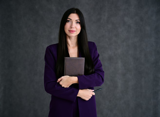 Portrait of a pretty brunette girl with good makeup with long hair on a gray background in a business suit with a folder in her hands. Stands in different poses with emotions.