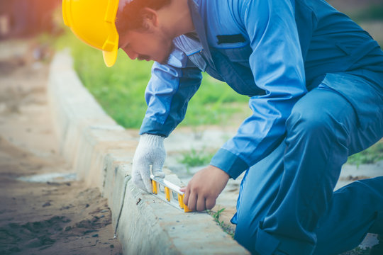 Asian civil engineer with Beard He wears the blue uniform worker and wears a yellow safety helmet. Using a plane measuring the pavement for road construction.