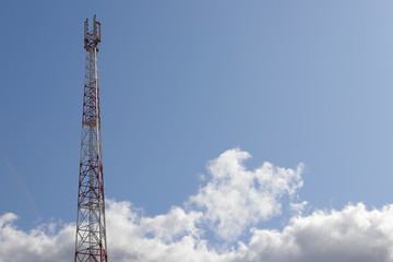 Telecommunications tower on light blue sky background and white club clouds