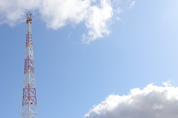 Obraz premium Telecommunications tower on light blue sky background and white club clouds