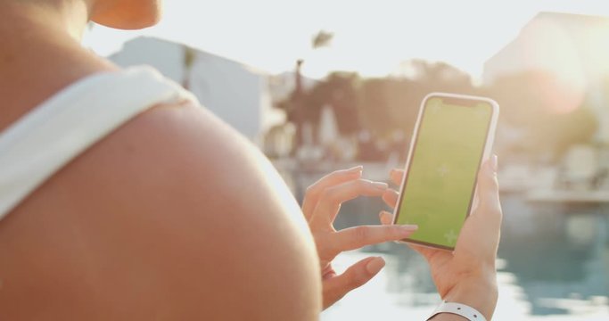 View over the shoulder of the young Caucasian woman who getting a sun tan at the swimming pool and using smartphone with chroma key and tracking motion. Green screen. Close up.