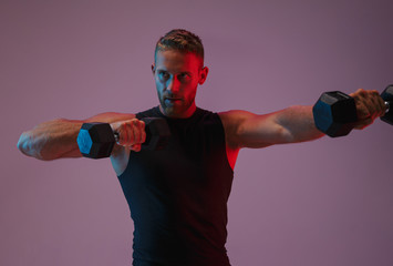 Concentrated young sports man make exercises with dumbbells.