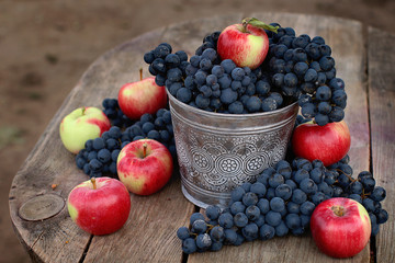Crowded bucket with tech blue grapes and apples on wooden background