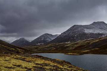 Mountain landscape. Rocky shore of a mountain lake on a rainy autumn day. First snow