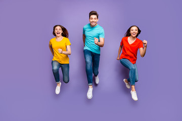 Full length body size front view photo of group of three crazy emotional hipsters models running to you wearing yellow blue t-shirts isolated violet background - obrazy, fototapety, plakaty