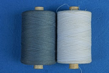 two bobbins with gray and white threads lie on a blue table