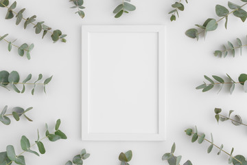 Top view of a white frame mockup surrounded by branches of eucalyptus on a white background.