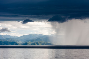 Storm with heavy rain and bright sun over the shore of lake Baikal