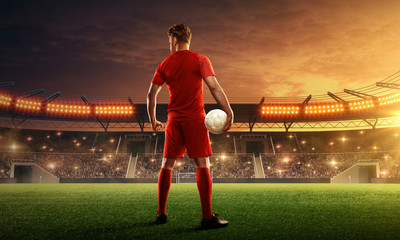 Soccer player on a floodlit and crowded soccer field with a ball. Dramatic night sky