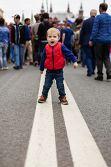 Naklejka premium Toddler screaming while standing on a dividing strip on the road, with many people behind