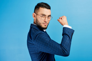 Kazakh Asian businessman in suit and glasses shows biceps, demonstrates his strength and power in...