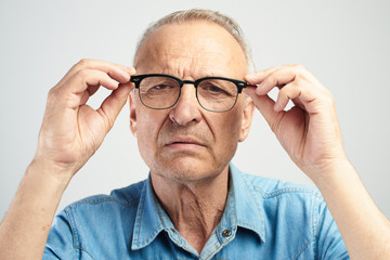Old man in eye glasses with diopters squints, stares intently at the camera isolated on a white...
