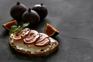 Toast with slices of figs on a wooden cutting board. Dark food photography.
