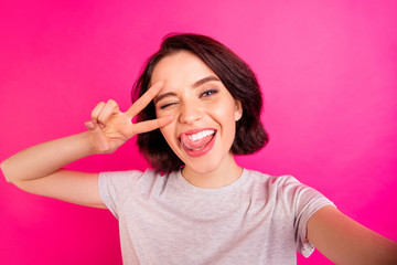 Self photo of charming cute nice attractive pretty sweet girlfriend licking her lips blinking taking selfie showing you v-sign near winking eye while isolated over pink color vivid background