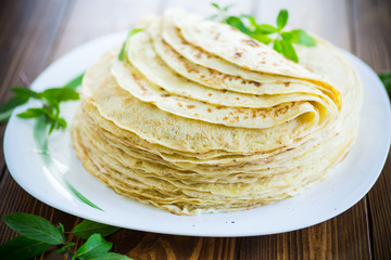many fried thin pancakes in a plate, on a table.