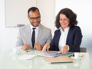 Cheerful business people signing contract. Smiling multiethnic businessman and businesswoman sitting at table and working with papers in office. Paperwork concept