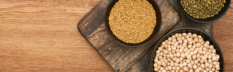 panoramic shot of bowls with grains and diverse legumes on wooden cutting boards