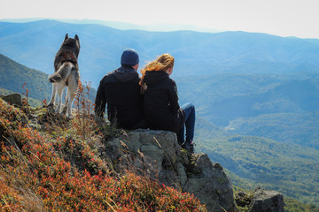 Cute couple in love in the autumn mountains.The couple sits on the edge of the mountain, stone. Siberian husky dog. Carpathian Mountains