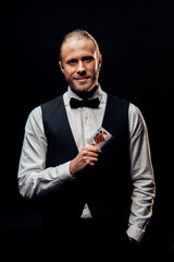 happy bearded croupier holding playing cards isolated on black
