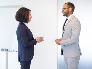 Smiling business people talking in office. Side view of cheerful multiethnic businessman and...