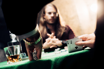 selective focus of man touching playing cards near player on black with smoke