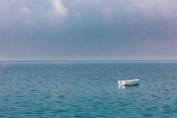 Lonely boat on calm sea on cloudy morning. Sea horizon with copy space